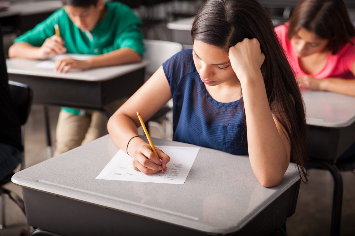 Jovem faz prova em uma sala com outros estudantes