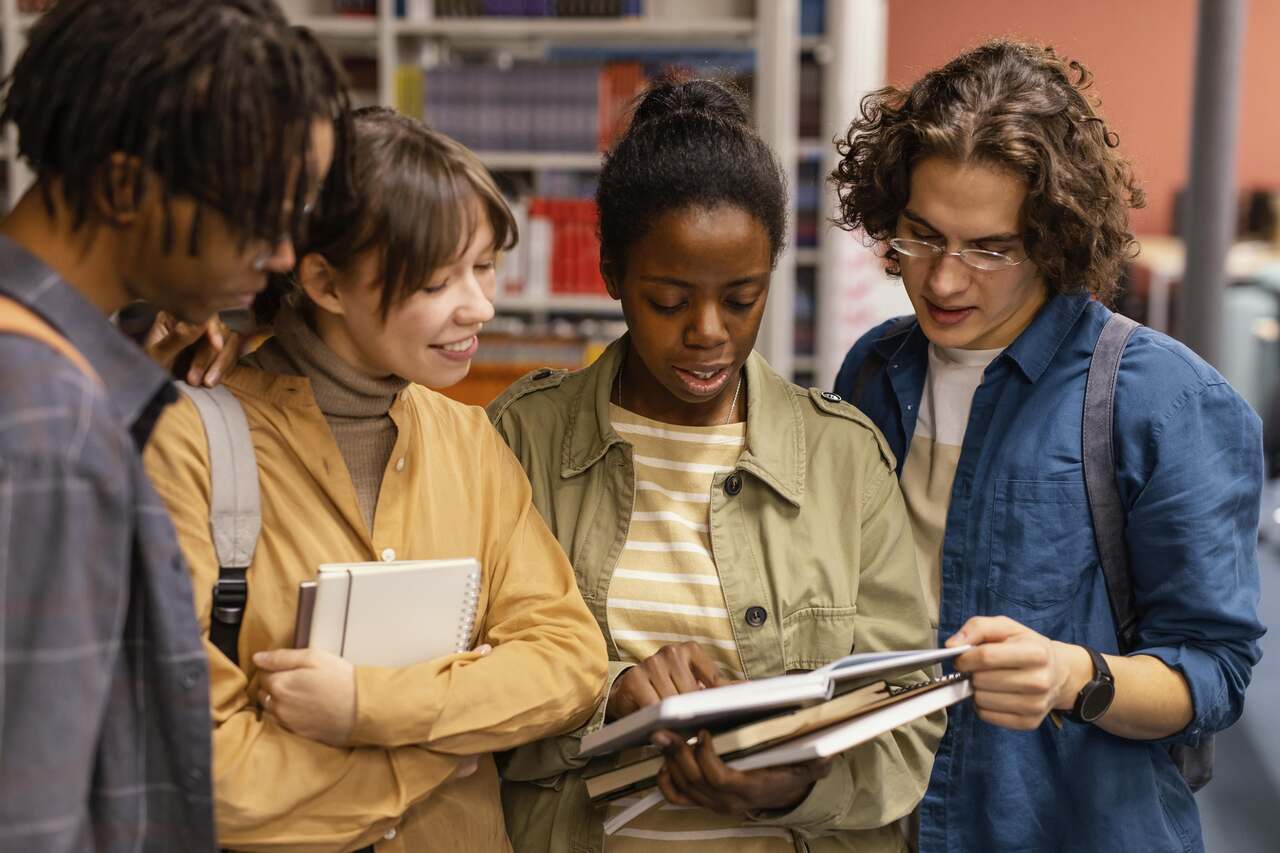 Grupo com 4 jovens lendo livros juntos em biblioteca
